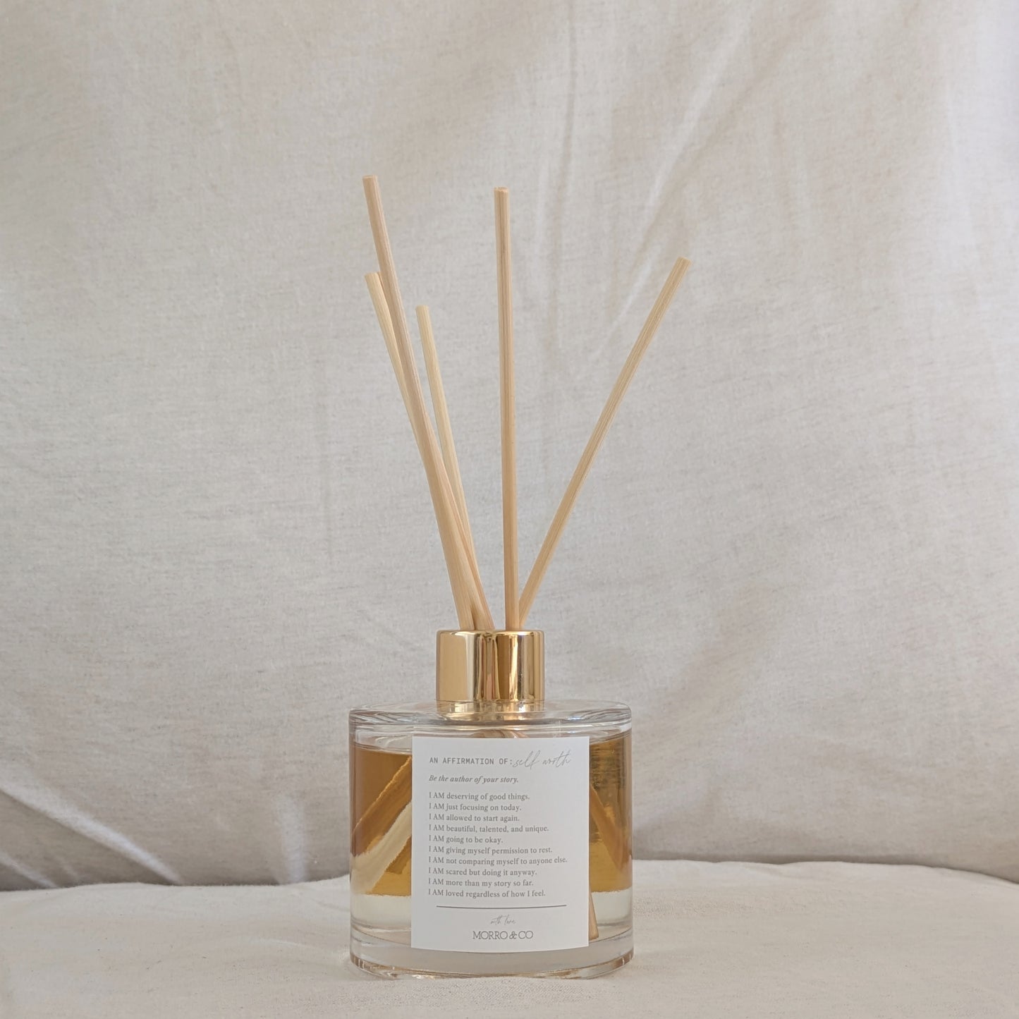 Reed diffuser with gold accents and positive affirmation on a neutral background
