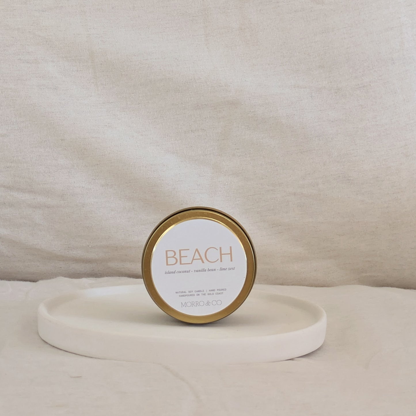 Gold candle travel tin labeled 'Beach' on a beige surface