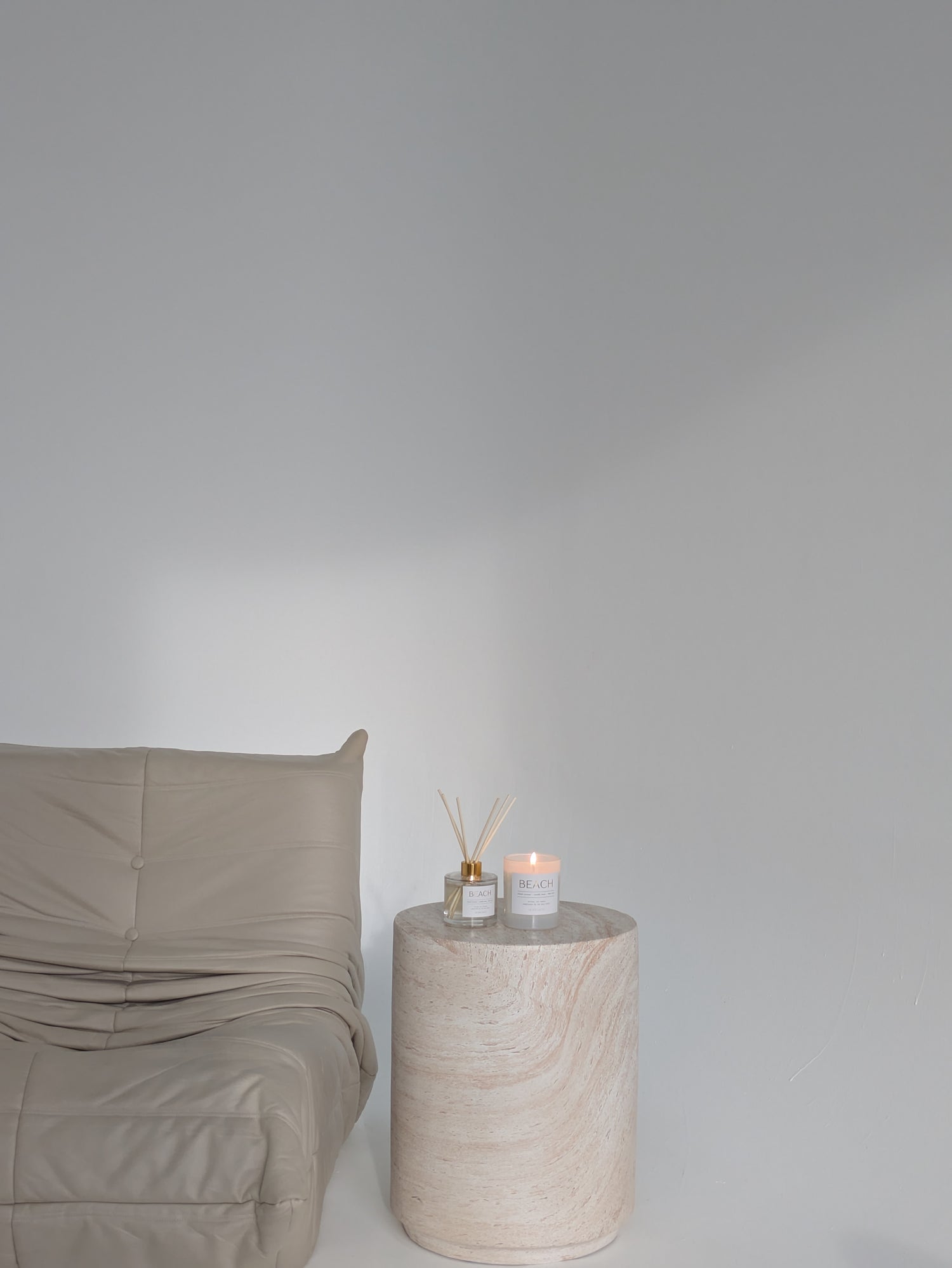 Beige cushion on a bed next to a round stone side table with a candle and plant.