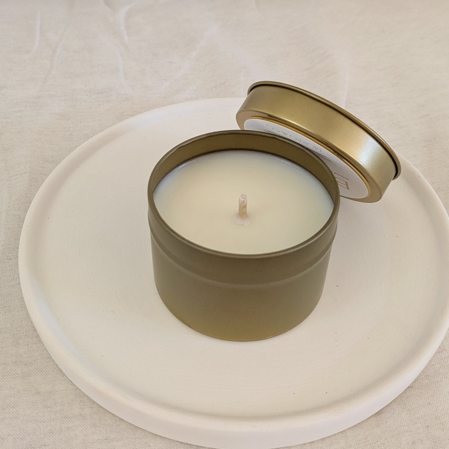 Candle in a gold travel tin with lid on a white plate