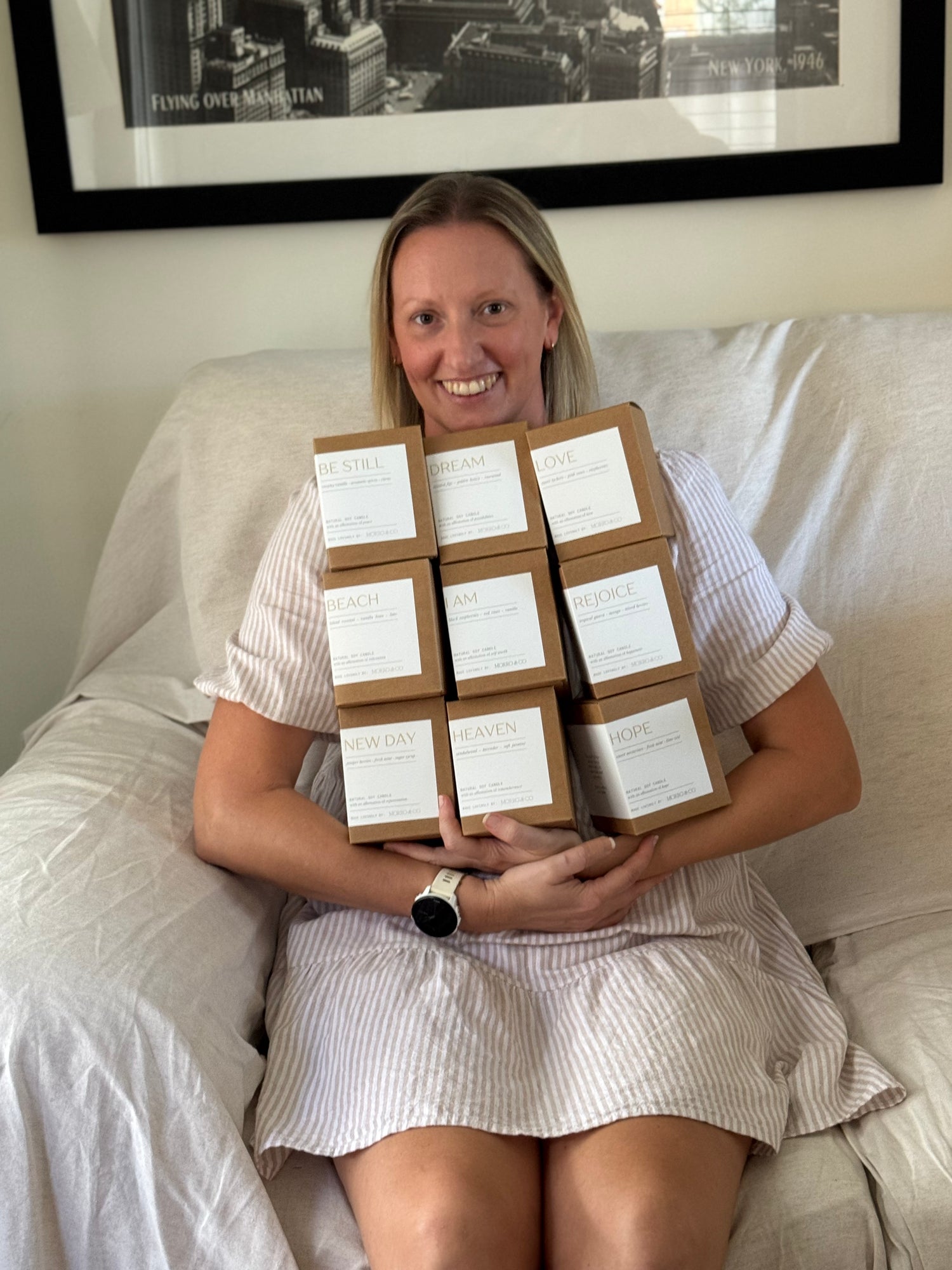 Woman sitting on a couch holding multiple boxes with labels.