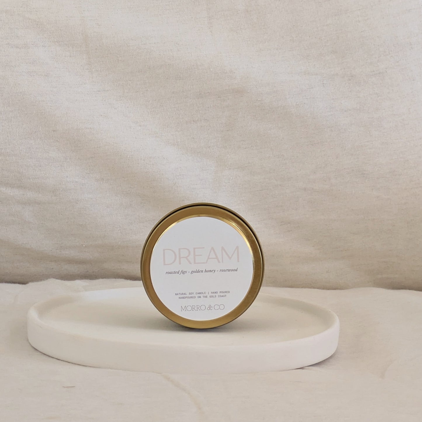 Gold candle travel tin labeled 'Dream' by Moro & Co on a beige background