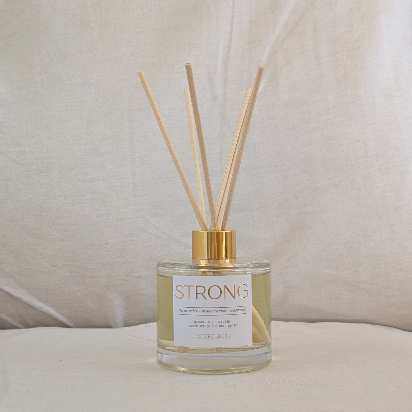 Eco reed diffuser with gold cap and 'STRONG' label on a neutral background