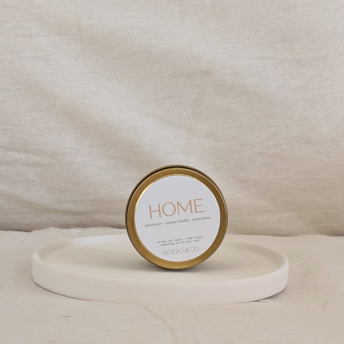 Candle gold travel tin labeled 'HOME' on a beige surface