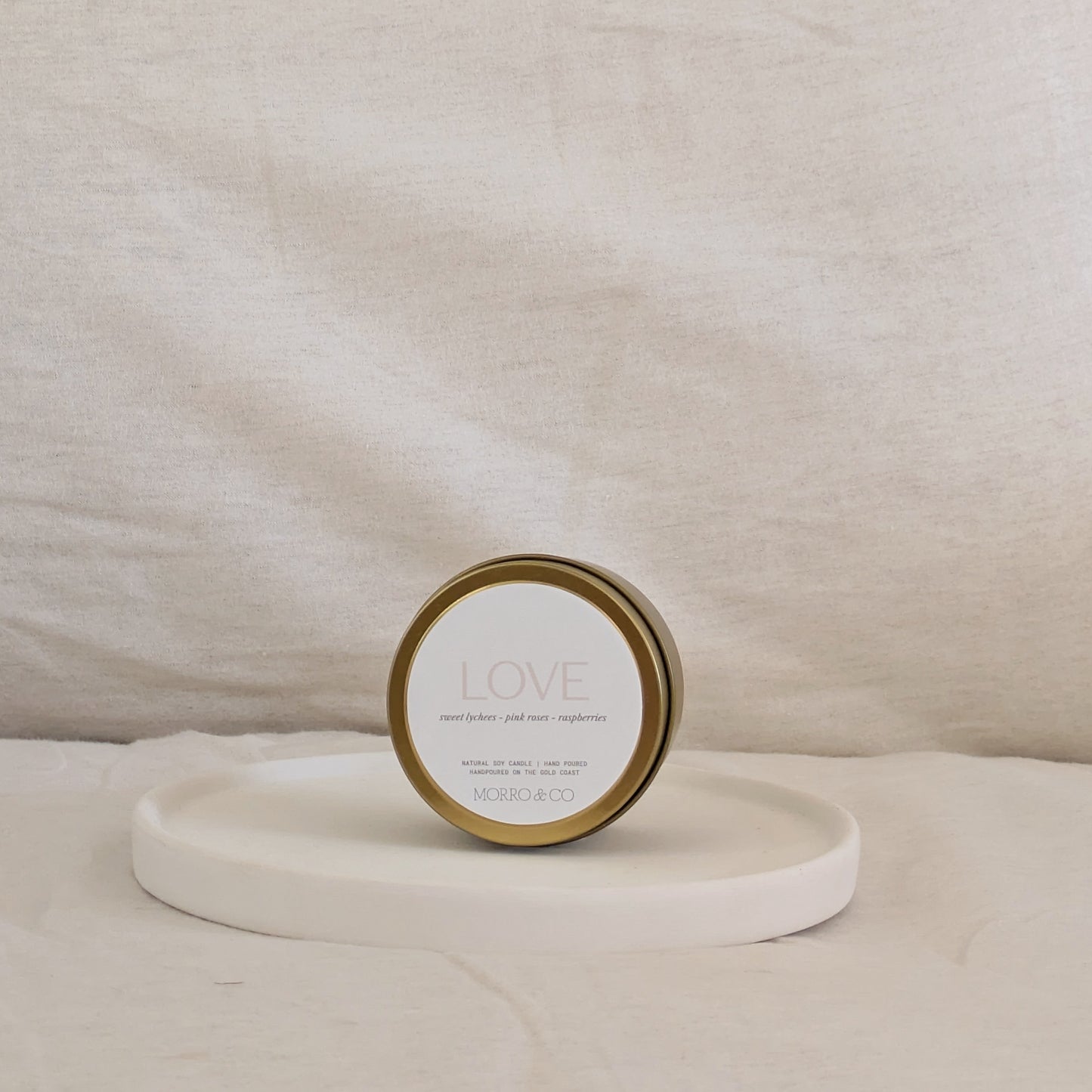 Gold candle travel tin labelled 'LOVE' on a white surface with a neutral background
