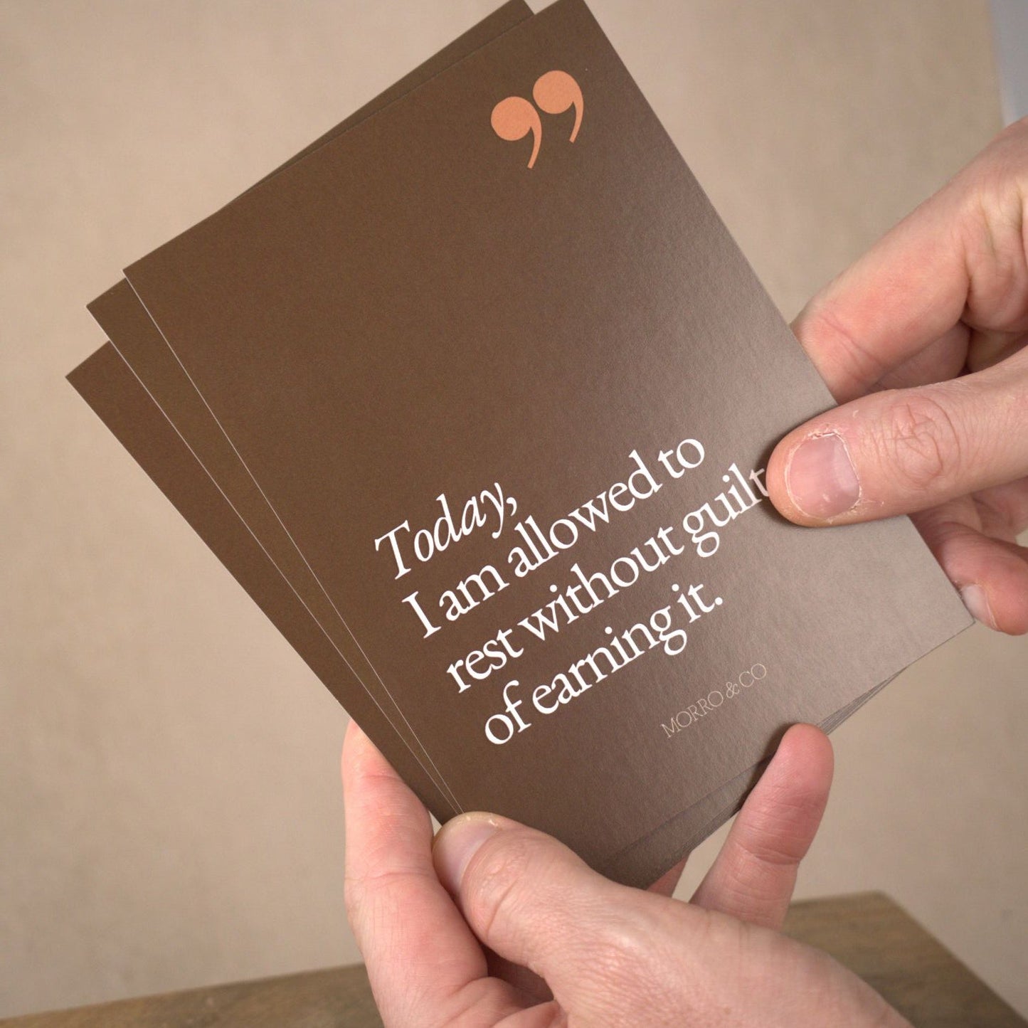 Hands holding a brown card with text and a logo on a beige background