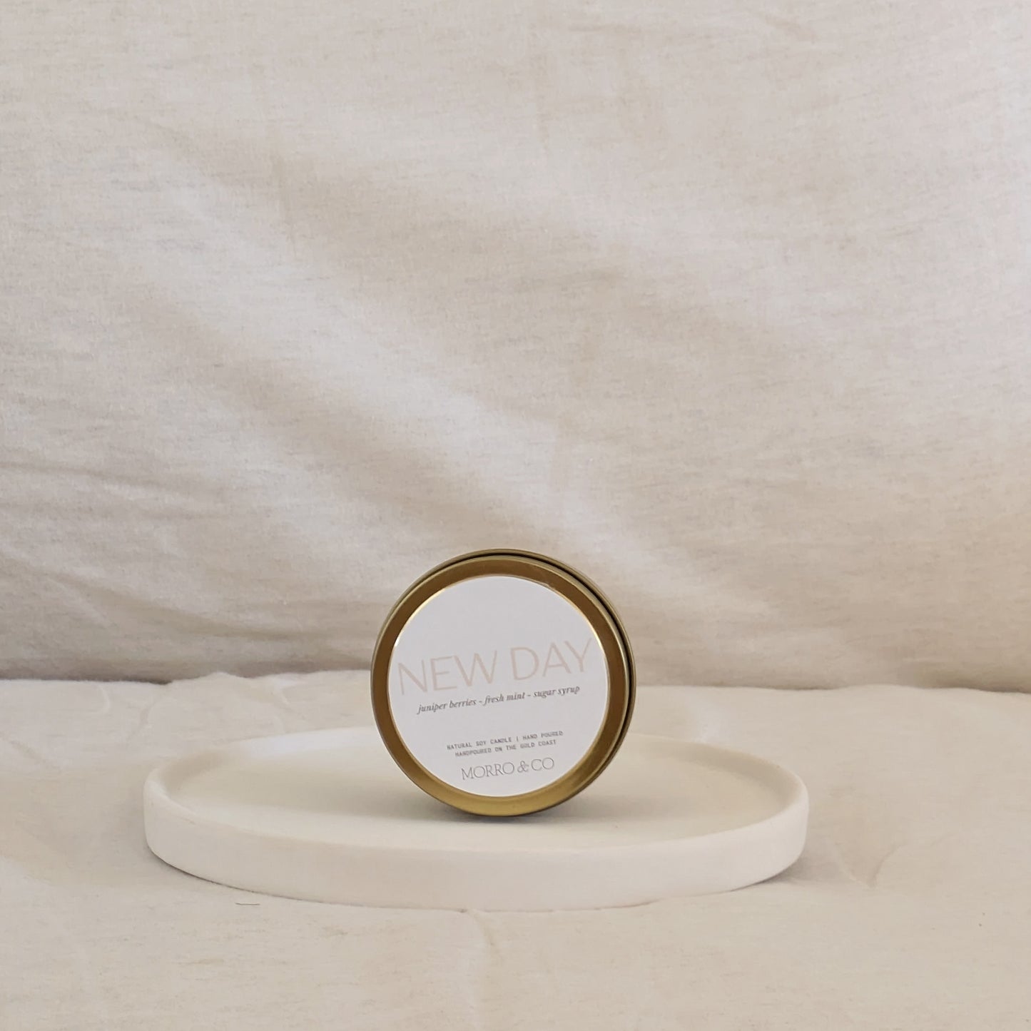 Gold candle travel tin labeled 'NEW DAY' on a white surface
