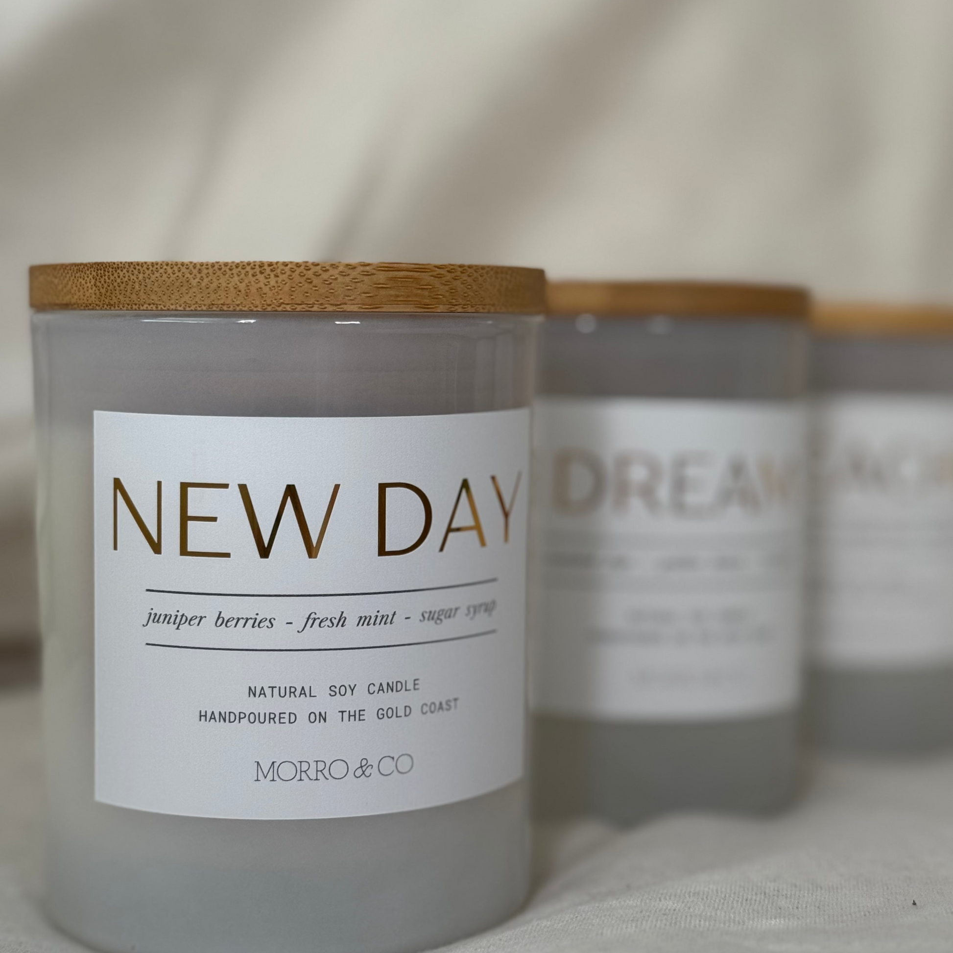 Candle labeled 'New Day' with a wooden lid on a neutral background