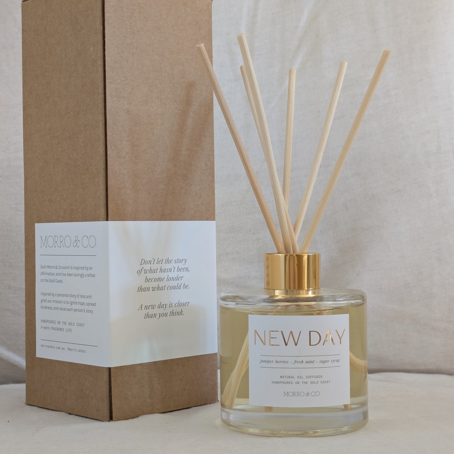 Diffuser bottle labeled 'New Day' with wooden sticks and a matching brown box on a neutral background