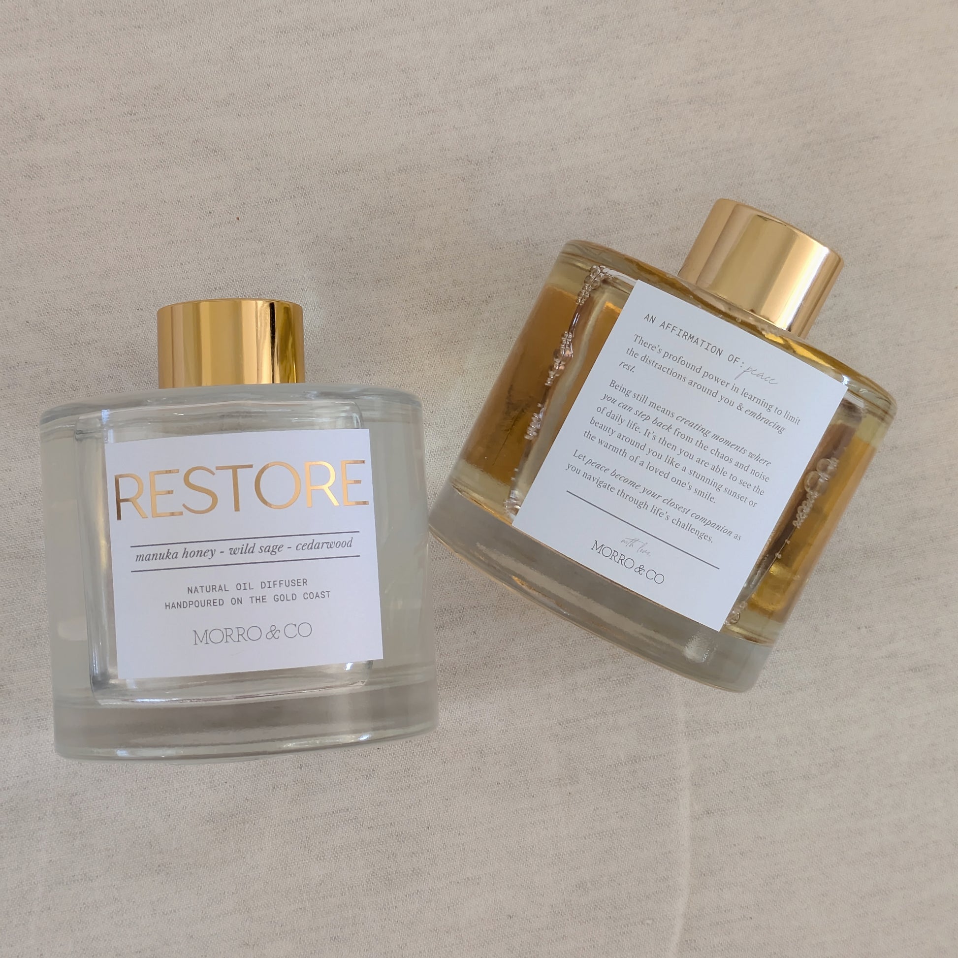 Two natural eco reed diffusers 
bottles of 'Restore' by Morro & Co on a beige background