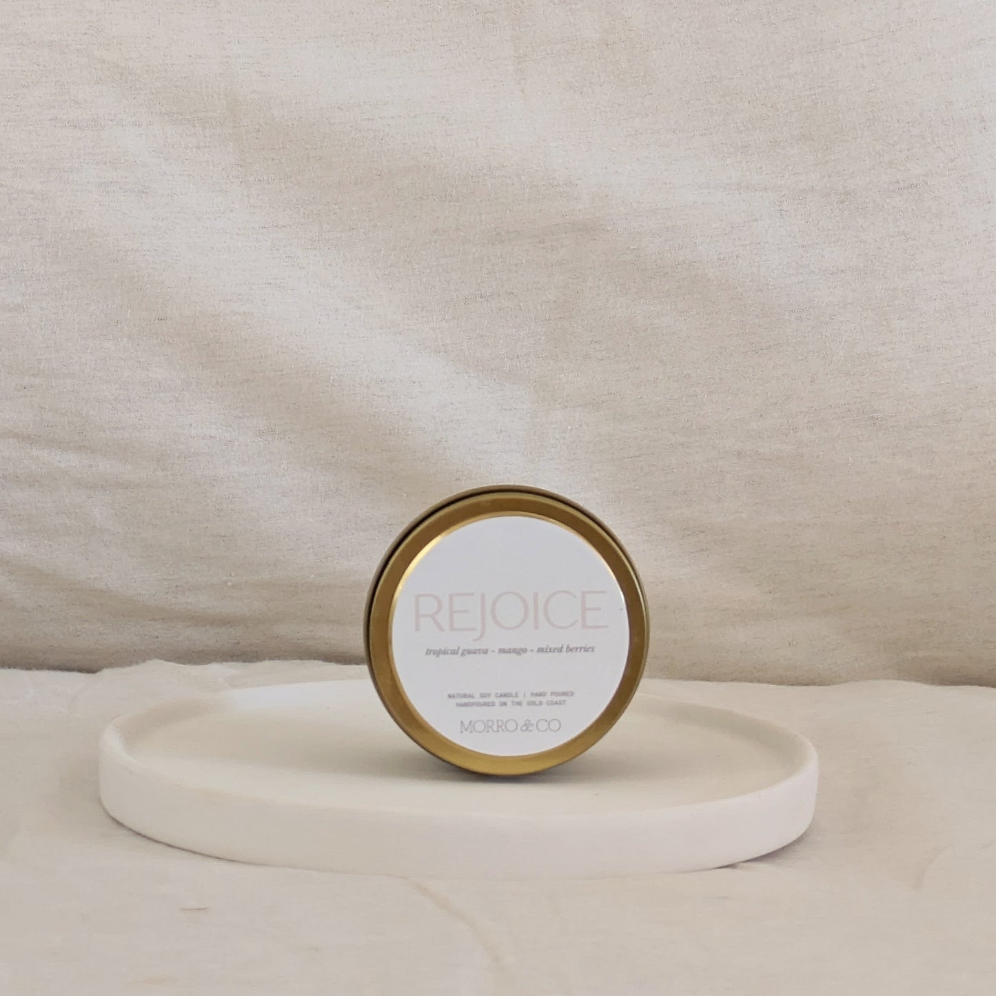 Gold candle travel tin 'Rejoice' on a beige surface