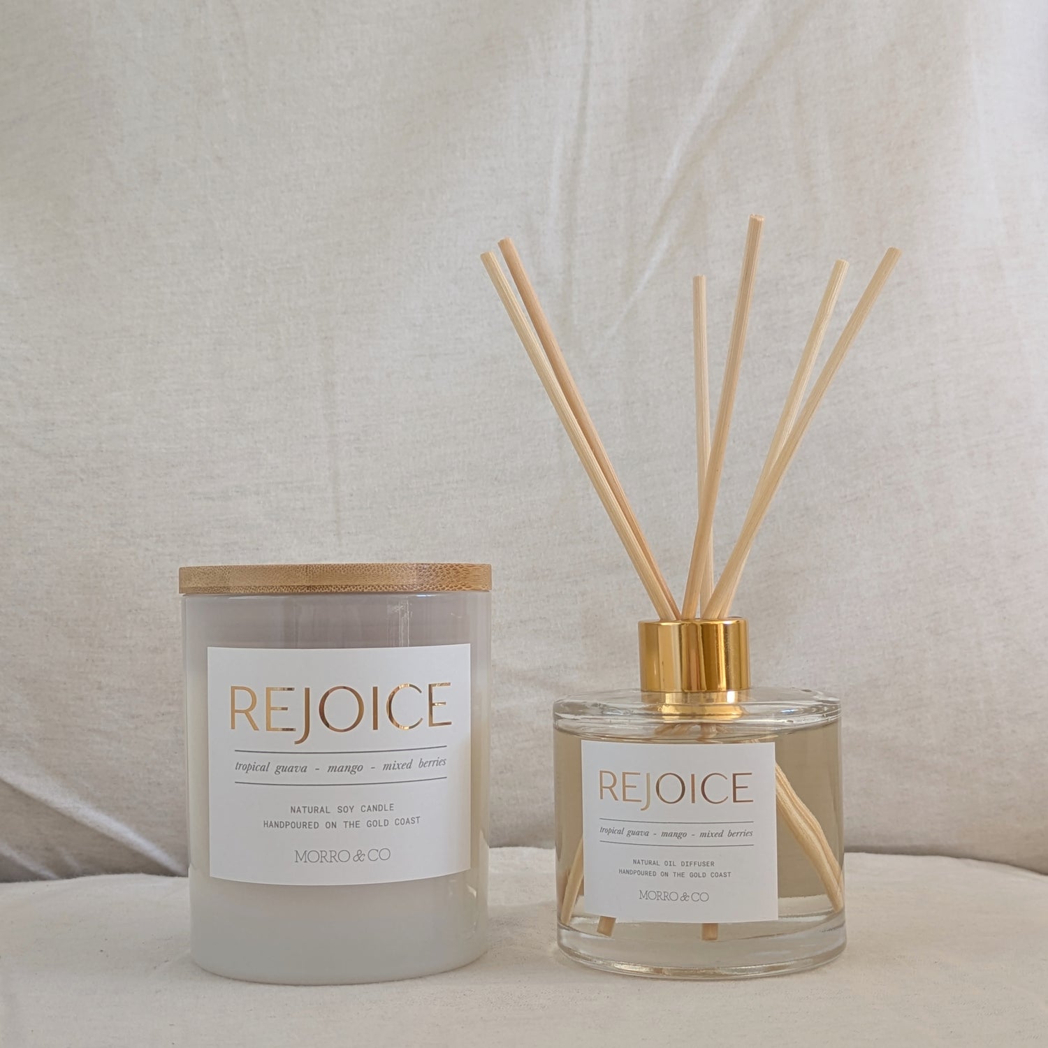 Two 'REJOICE' products, a candle and a diffuser, on a neutral background.