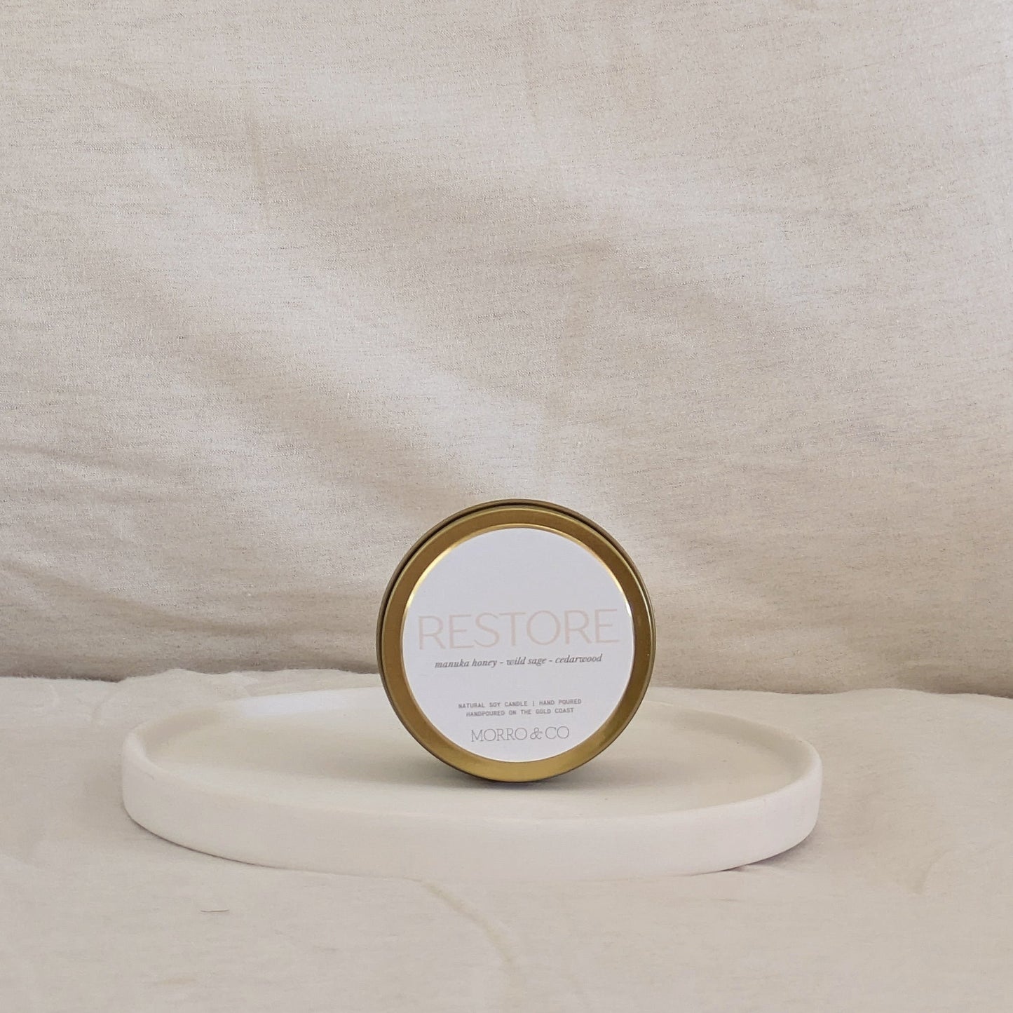 Candle gold travel tin labeled 'RESTORE' on a beige surface
