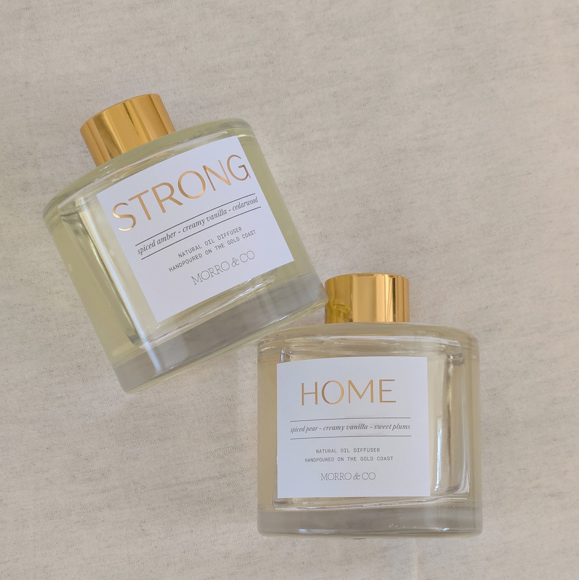 Two natural eco reed diffuser bottles labeled 'STRONG' and 'HOME' on a beige background
