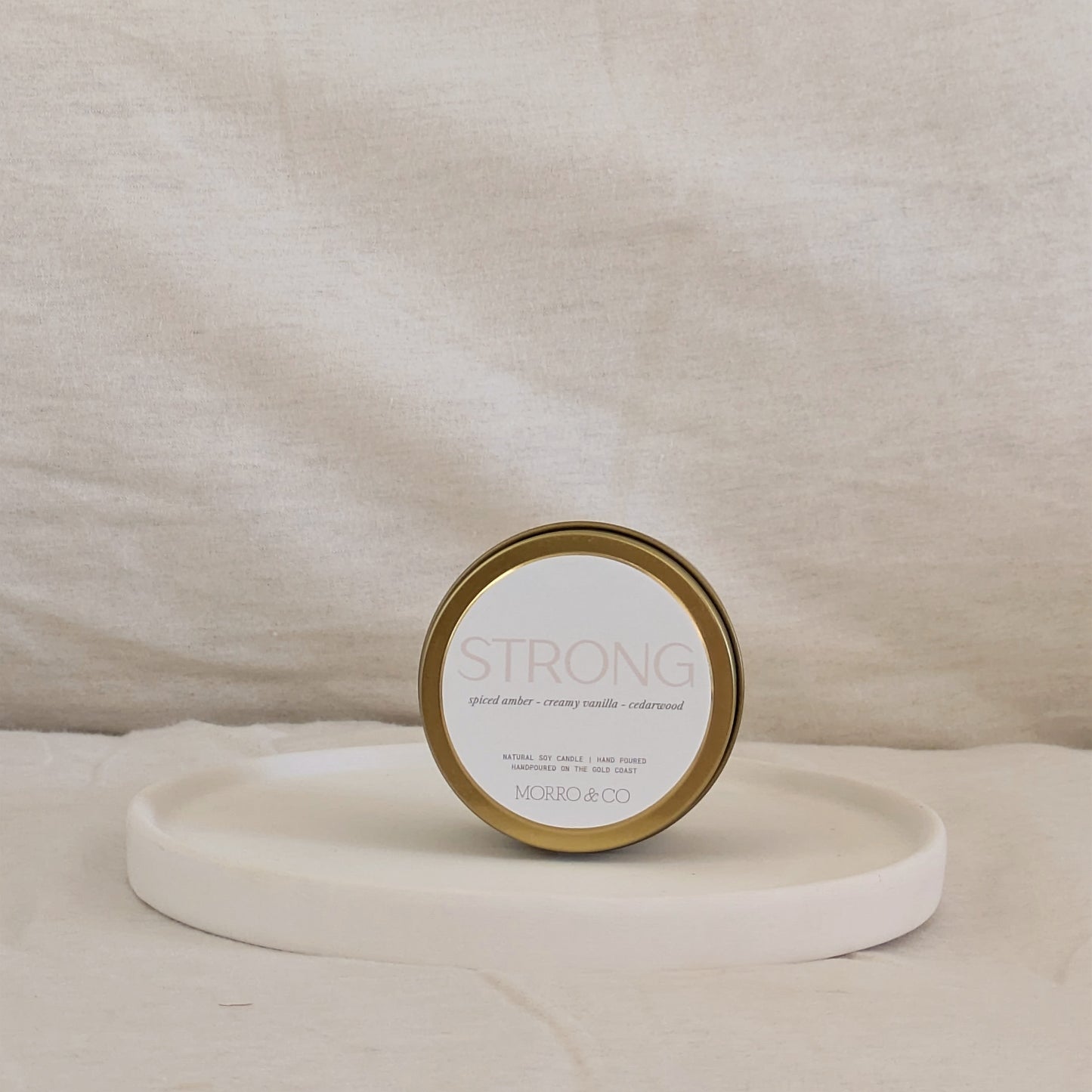 Gold candle travel tin labeled 'STRONG' on a beige surface