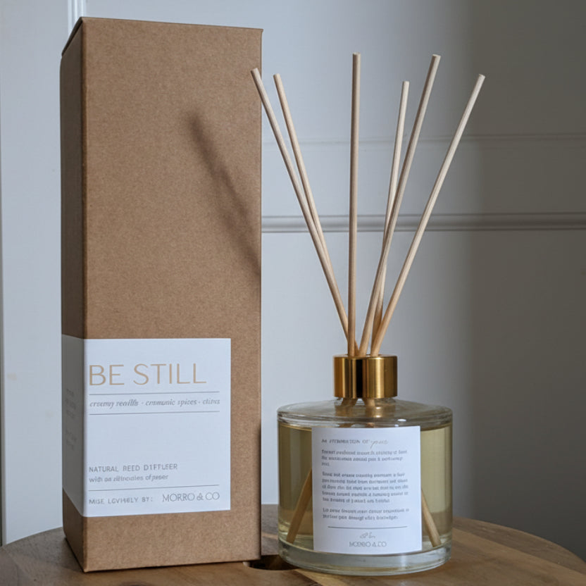 Diffuser bottle and packaging with 'Be Still' text on a wooden surface.
