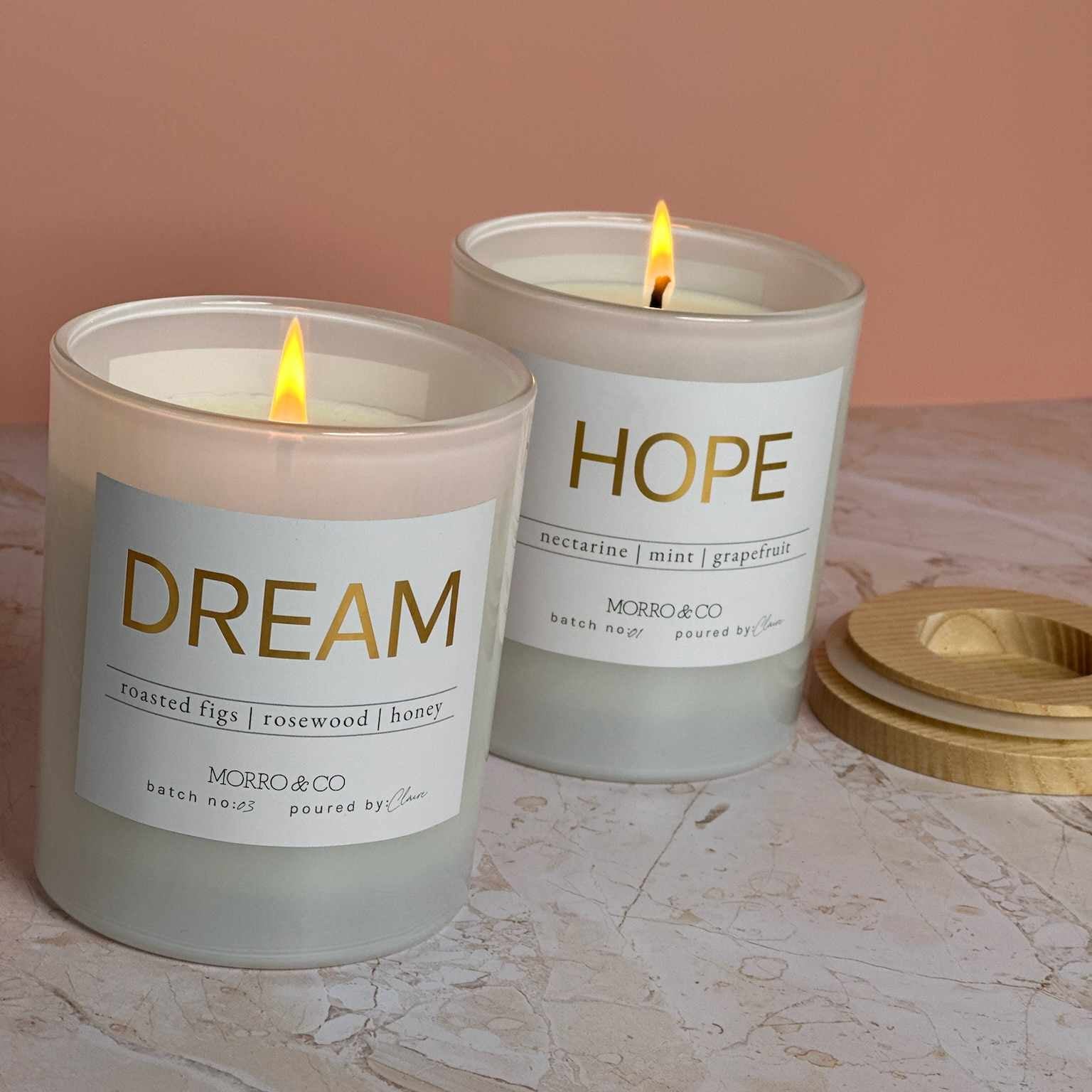 Two lit candles labeled 'Dream' and 'Hope' on a marble surface with a pinkish-beige background.