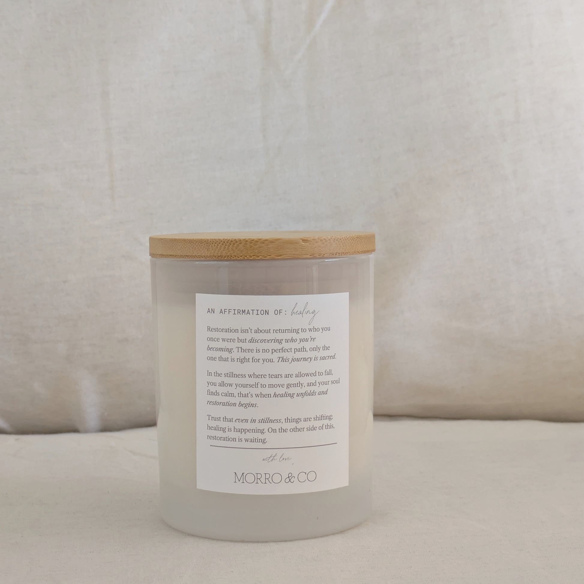 Back of RESTORE candle with a wooden lid and affirmation label on a beige background