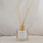 Reed diffuser labeled 'Beach' with a gold cap on a neutral background