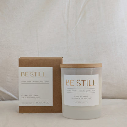 Candle and packaging with 'BE STILL' text on a neutral background