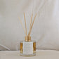 Natural eco reed diffuser with wooden sticks in a glass bottle, affirmation label on a neutral background