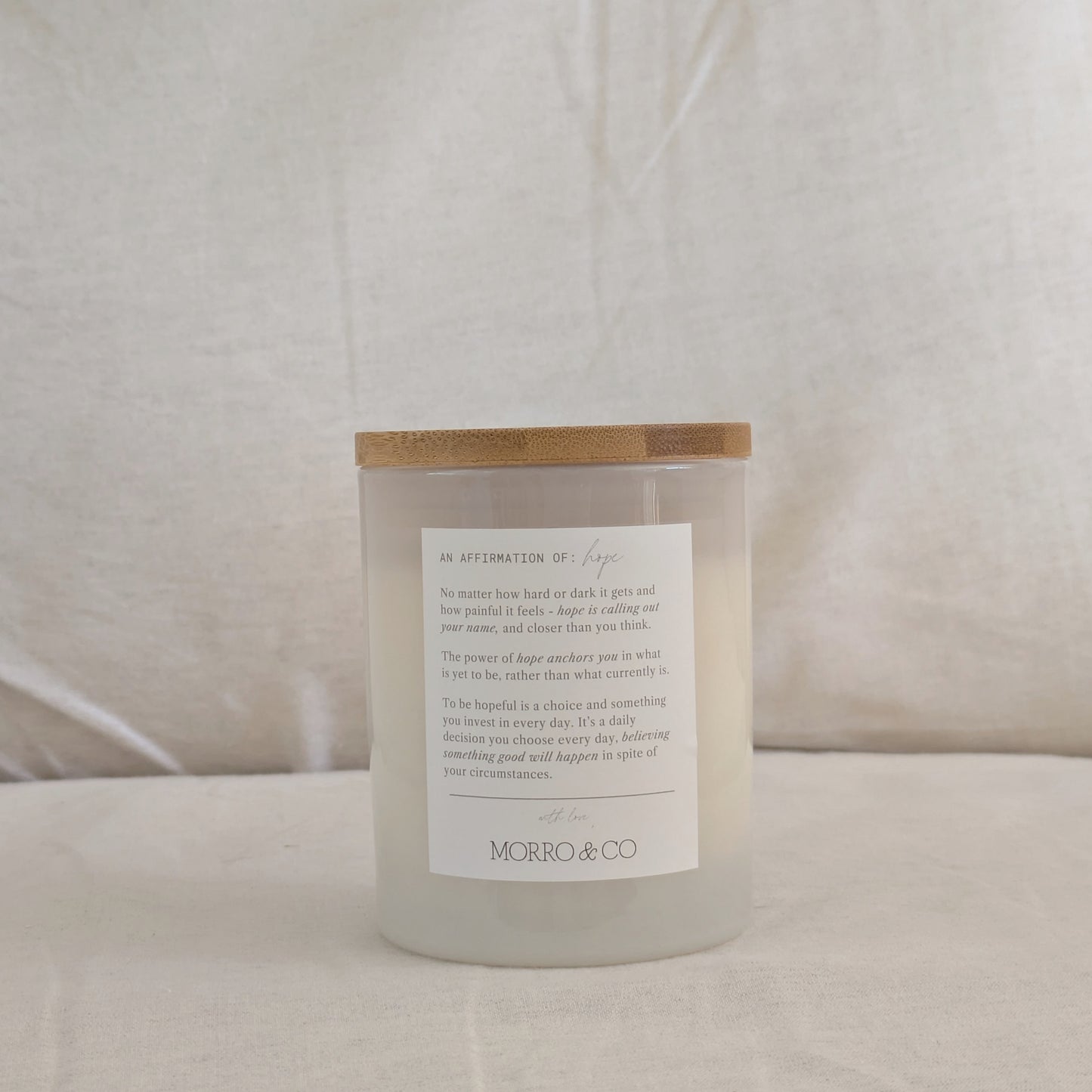 Back of HOPE candle with a wooden lid and affirmation label on a neutral background
