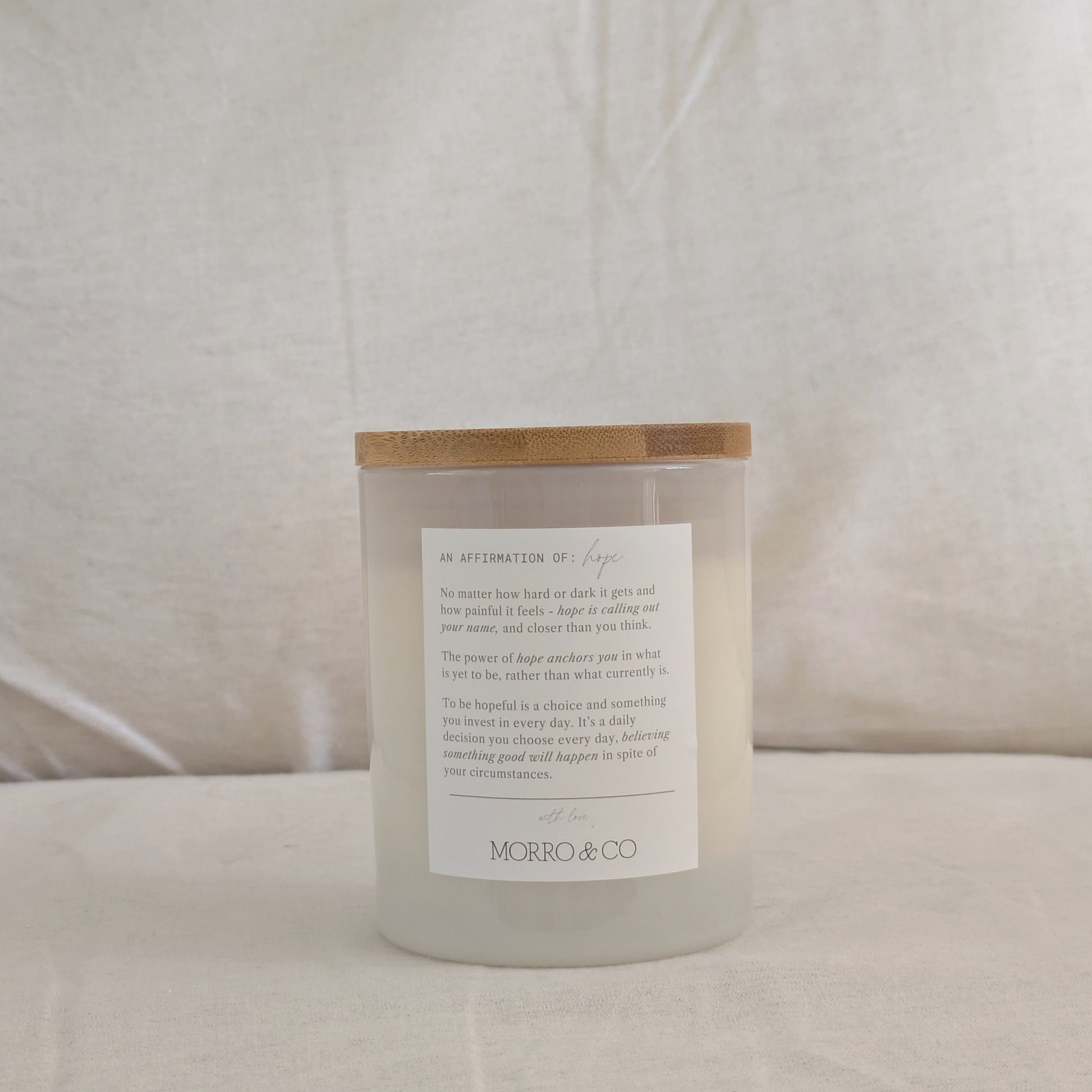 Back of HOPE candle with a wooden lid and affirmation label on a neutral background