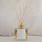Natural eco reed diffuser with gold cap and clear container, affirmation label on a neutral background