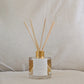 Reed eco reed diffuser with gold cap, affirmation label and clear container on a neutral background