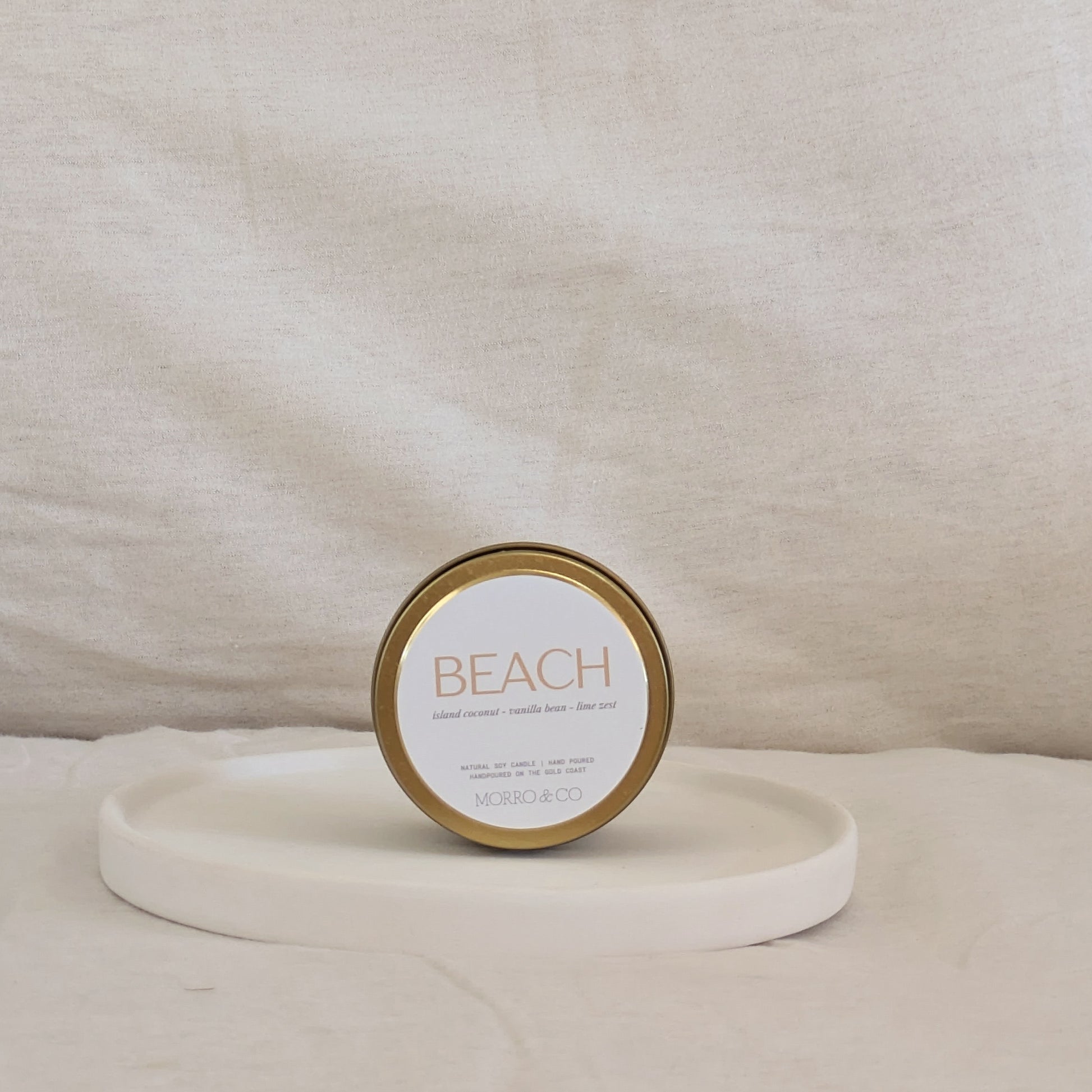 Gold candle travel tin labeled 'Beach' on a beige surface