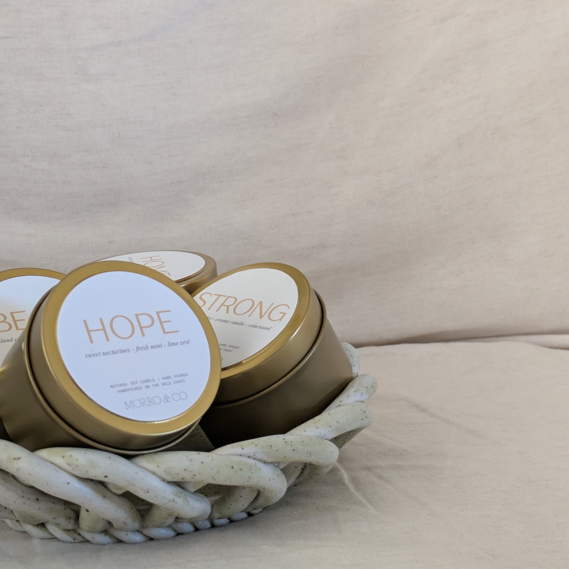 Gold candle travel tins with 'HOPE' and 'STRONG' on a beige surface