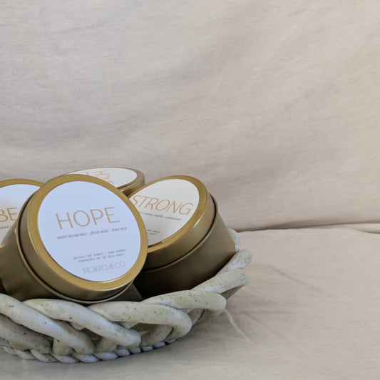 Gold candle travel tins with 'HOPE' and 'STRONG' on a beige surface