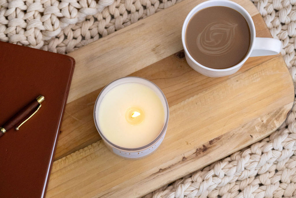 Candle and mug on a wooden tray with a textured beige surface
