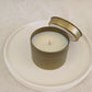 Candle in a gold travel tin with lid on a white plate