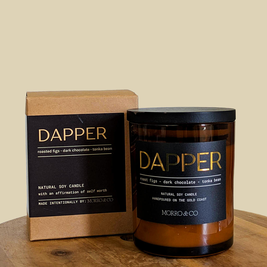 Dapper candle and packaging on a wooden surface with a beige background