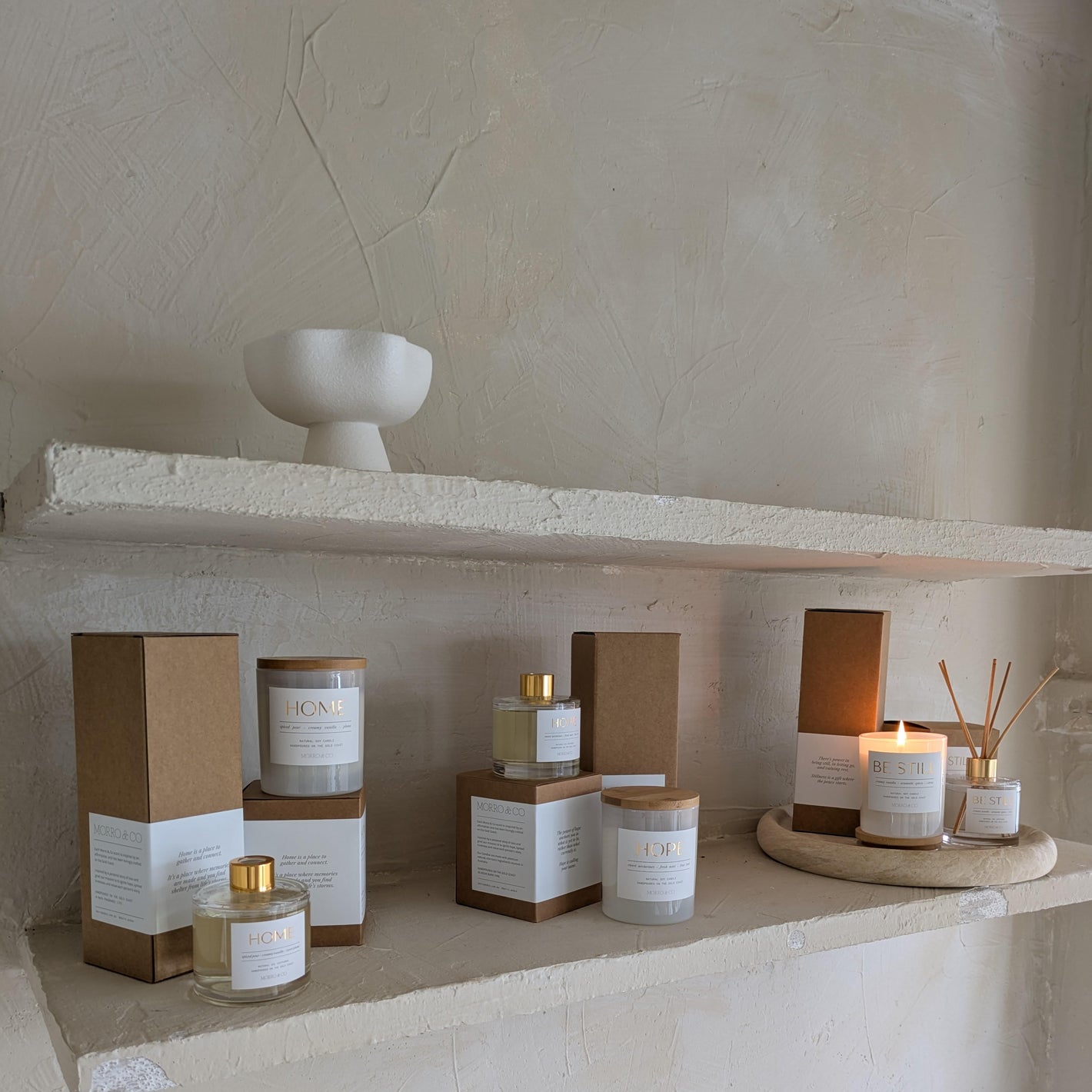Candle and diffuser products on a stone shelf with a neutral background