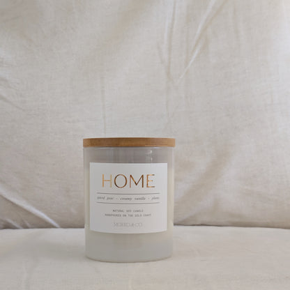 Front of HOME candle with a wooden lid and 'HOME' gold label on a beige background