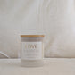 Front of candle with a wooden lid labeled with a gold label 'LOVE' on a beige fabric background