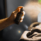 Hand holding a spray bottle labeled 'Jalo' over a person's head, with a blurred background.