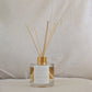 Natural eco reed diffuser with gold cap, affirmation label and clear bottle on a neutral background