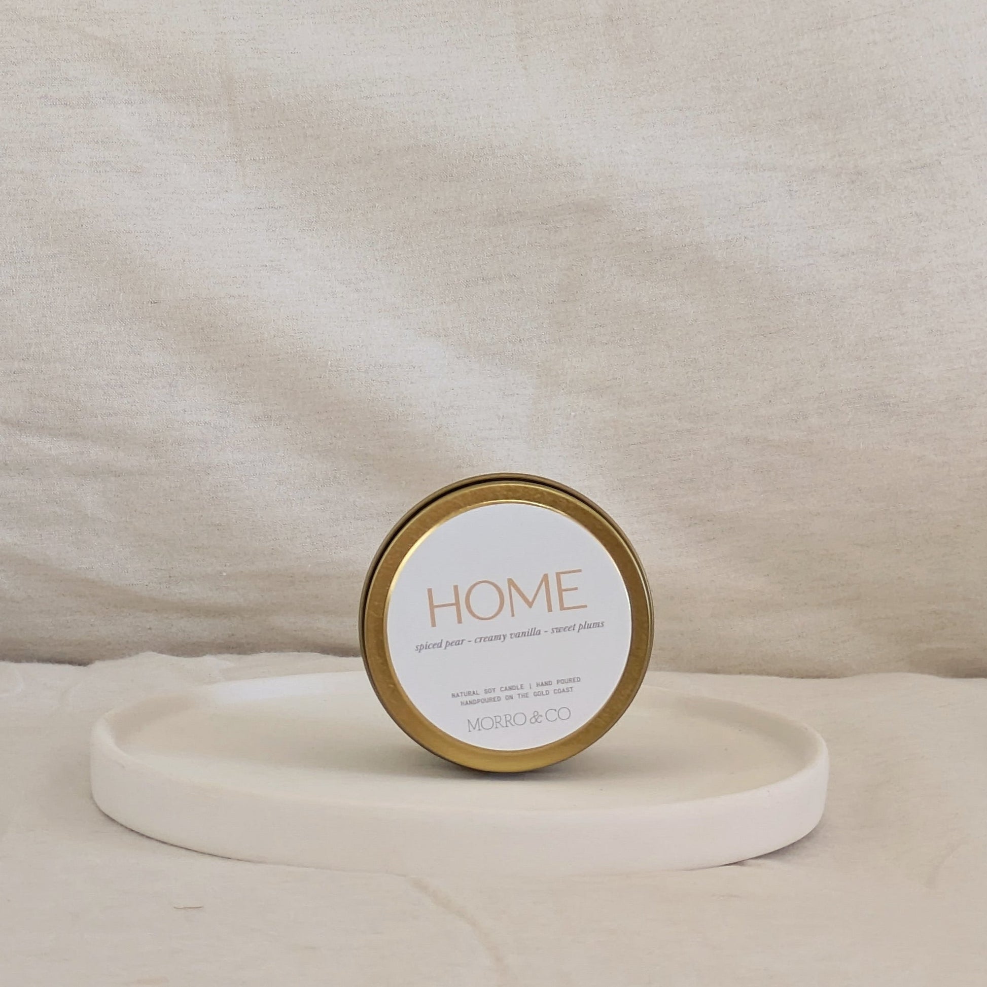Candle gold travel tin labeled 'HOME' on a beige surface
