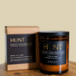 Hunt candle and packaging on a wooden surface with a beige background