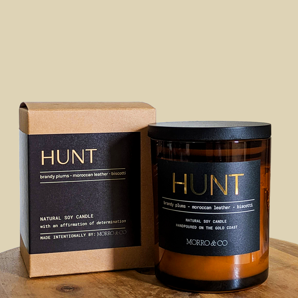 Hunt candle and packaging on a wooden surface with a beige background