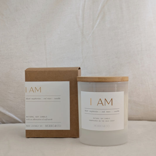 Candle and packaging with 'I AM' label on a neutral background