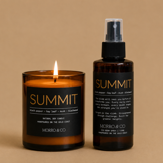 A lit amber glass candle and an amber spray bottle with black labels, both branded SUMMIT by MORRO & CO, set against a solid beige background.