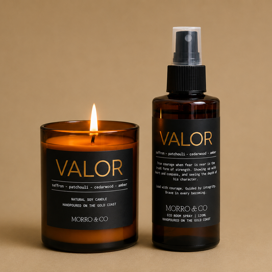 A lit amber glass jar candle and a matching amber spray bottle labeled VALOR by MORRO & CO, set against a solid beige background.