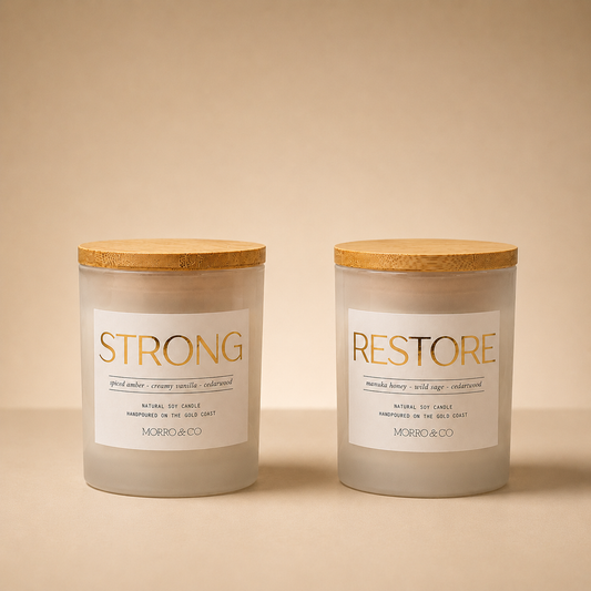 Morro & Co Two candles labeled 'Strong' and 'Restore' with wooden lids on a beige background.