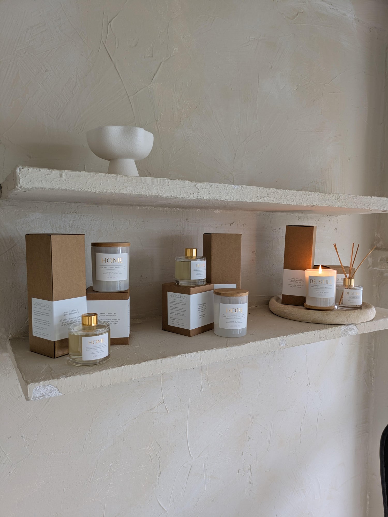 Candle and diffuser products on a stone shelf with a neutral background