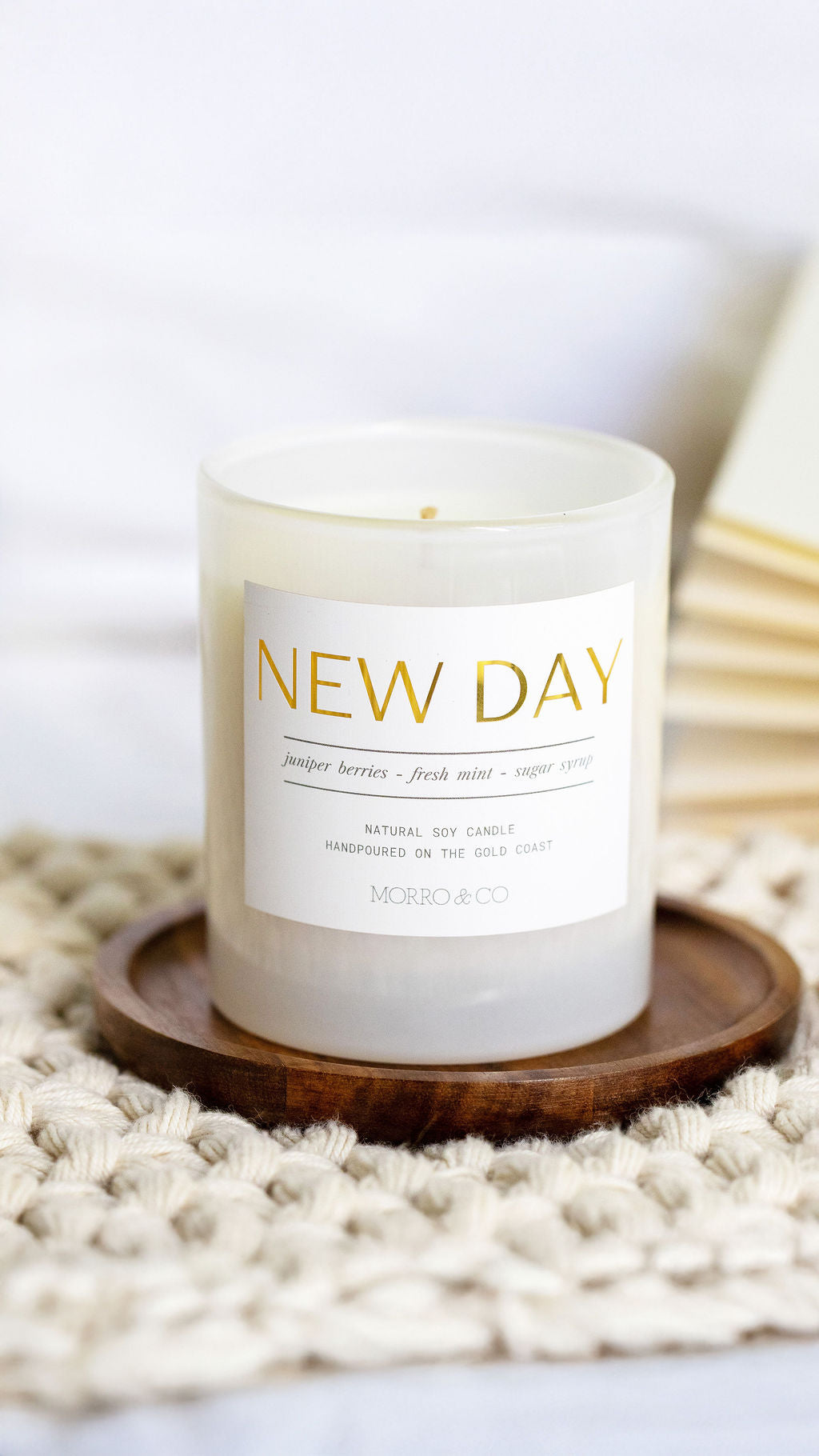 Candle labeled 'New Day' on a wooden coaster with a white background