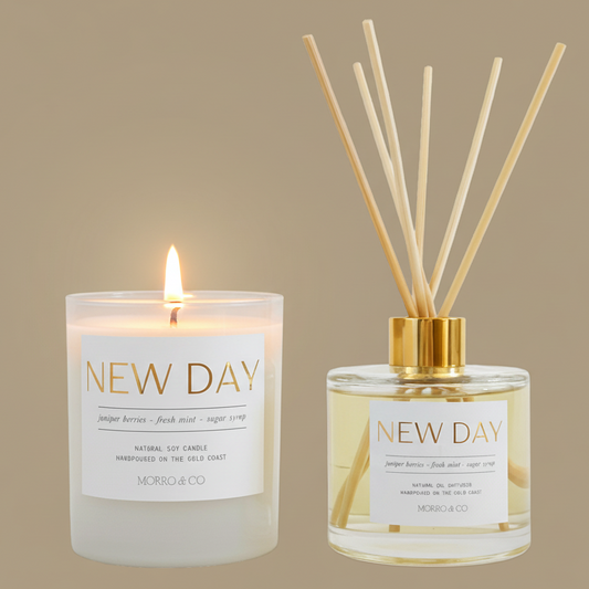 Two 'New Day' products, a candle and a diffuser, on a beige background.